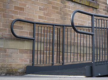Shows an image of a ramp that aims to show off the trombone ends on the ends of the rails to stop clothes and bags snagging. The ramp is against a brick wall.
