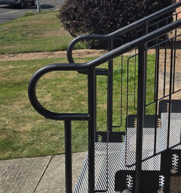 Black metal handrails with curved trombone ends fitted to outdoor access steps, showing smooth continuous design for safer grip and reduced snagging.