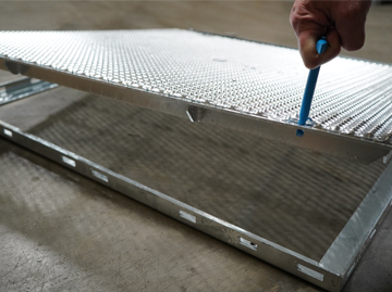 Man lifting up a hatch section of a metal mesh platform using a blue tool.